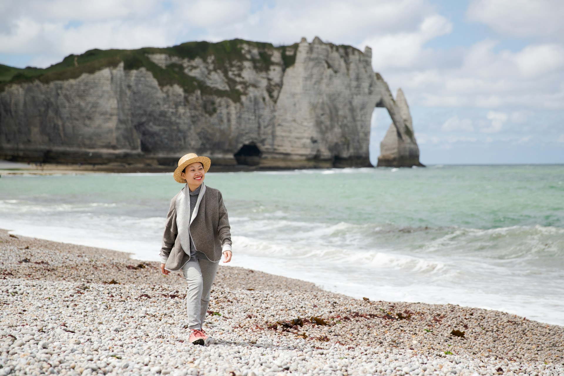 Asian woman in France in front of the Etretat Aval cliff, rocks and natural arch landmark by blue ocean