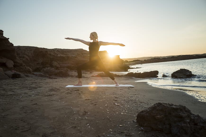 Greece, Crete, woman practicing yoga on the beach at sunset