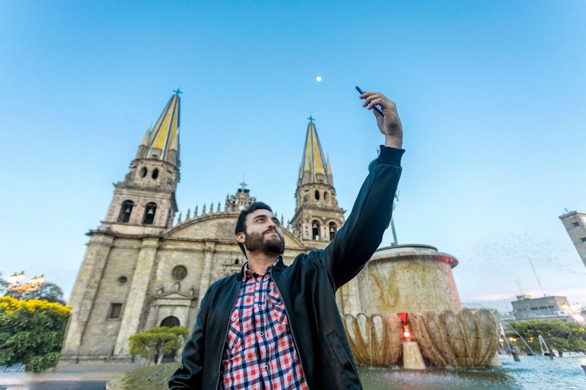 Young tourist taking a selfie with his cell phone in the Cathedral in the city of Guadalajara, Jalisco, Mexico.; Shutterstock ID 1404021563; your: Sloane Tucker; gl: 65050; netsuite: Online Editorial; full: Guadalajara Neighborhoods Article
