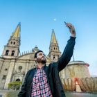 Young tourist taking a selfie with his cell phone in the Cathedral in the city of Guadalajara, Jalisco, Mexico.; Shutterstock ID 1404021563; your: Sloane Tucker; gl: 65050; netsuite: Online Editorial; full: Guadalajara Neighborhoods Article