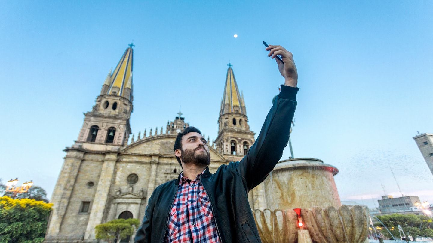 Young tourist taking a selfie with his cell phone in the Cathedral in the city of Guadalajara, Jalisco, Mexico.; Shutterstock ID 1404021563; your: Sloane Tucker; gl: 65050; netsuite: Online Editorial; full: Guadalajara Neighborhoods Article