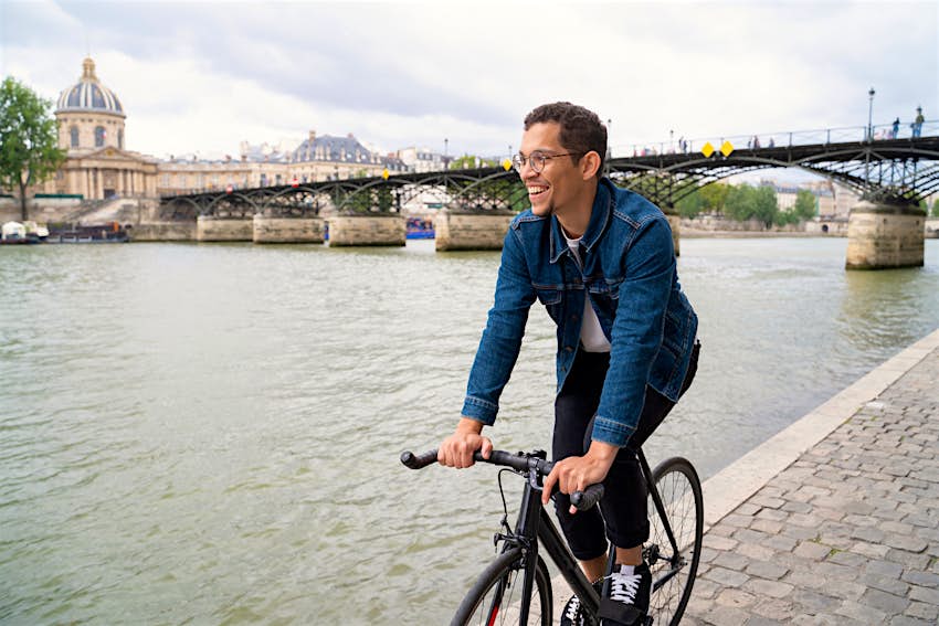 Smiling man riding bike on the walkway near to Seine river.