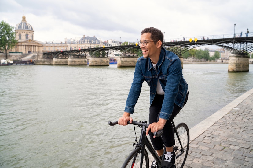 Smiling man riding bike on the walkway near to Seine river.