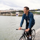 Smiling man riding bike on the walkway near to Seine river.