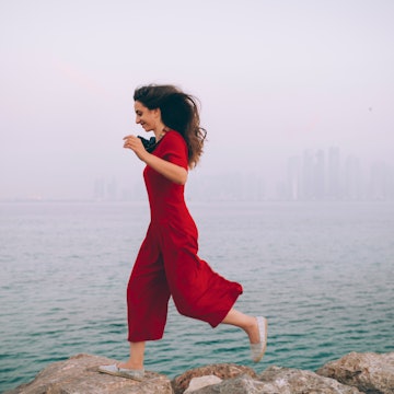 Woman Jumping Over The Rocks In Foggy Morning At The Seaside