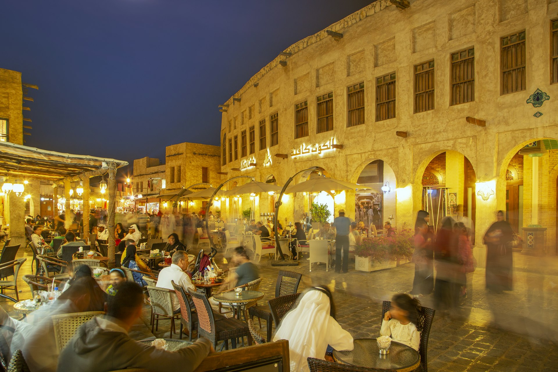 Illuminated traditional houses and people in outdoor restaurants in the historical district of Doha.