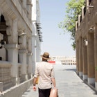 Walking in Souq Waqif, Doha, Qatar. Wearing vintage travel outfit, light brown fedora, linen shirt and carrying vintage suitcase. Feeling of adventure travel and nostalgia. Arabic, Middle Eastern set.; Shutterstock ID 1932801596; your: Sloane Tucker; gl: 65050; netsuite: Online editorial; full: Qatar on a budget article