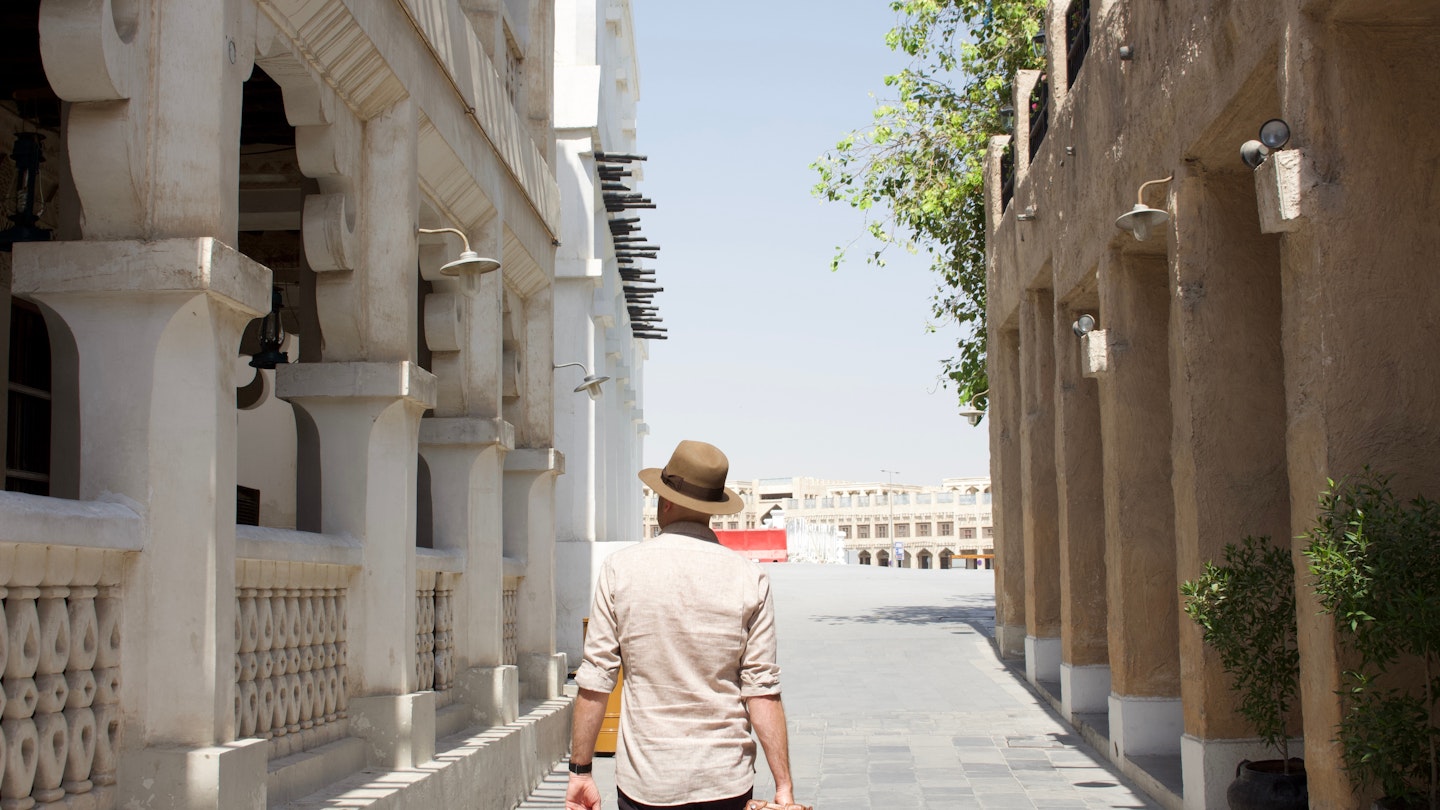 Walking in Souq Waqif, Doha, Qatar. Wearing vintage travel outfit, light brown fedora, linen shirt and carrying vintage suitcase. Feeling of adventure travel and nostalgia. Arabic, Middle Eastern set.; Shutterstock ID 1932801596; your: Sloane Tucker; gl: 65050; netsuite: Online editorial; full: Qatar on a budget article