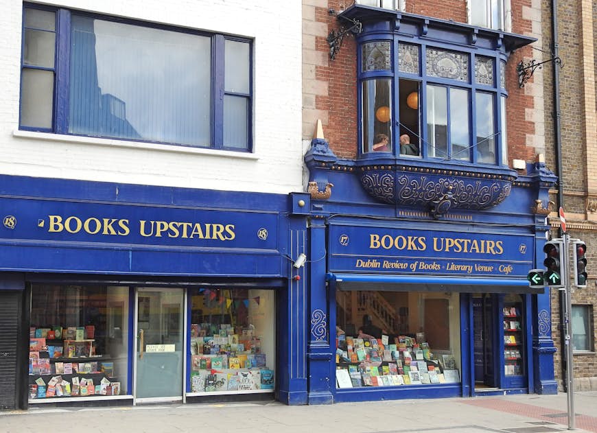 The blue fascade of a bookstore titled "Books Upstairs"