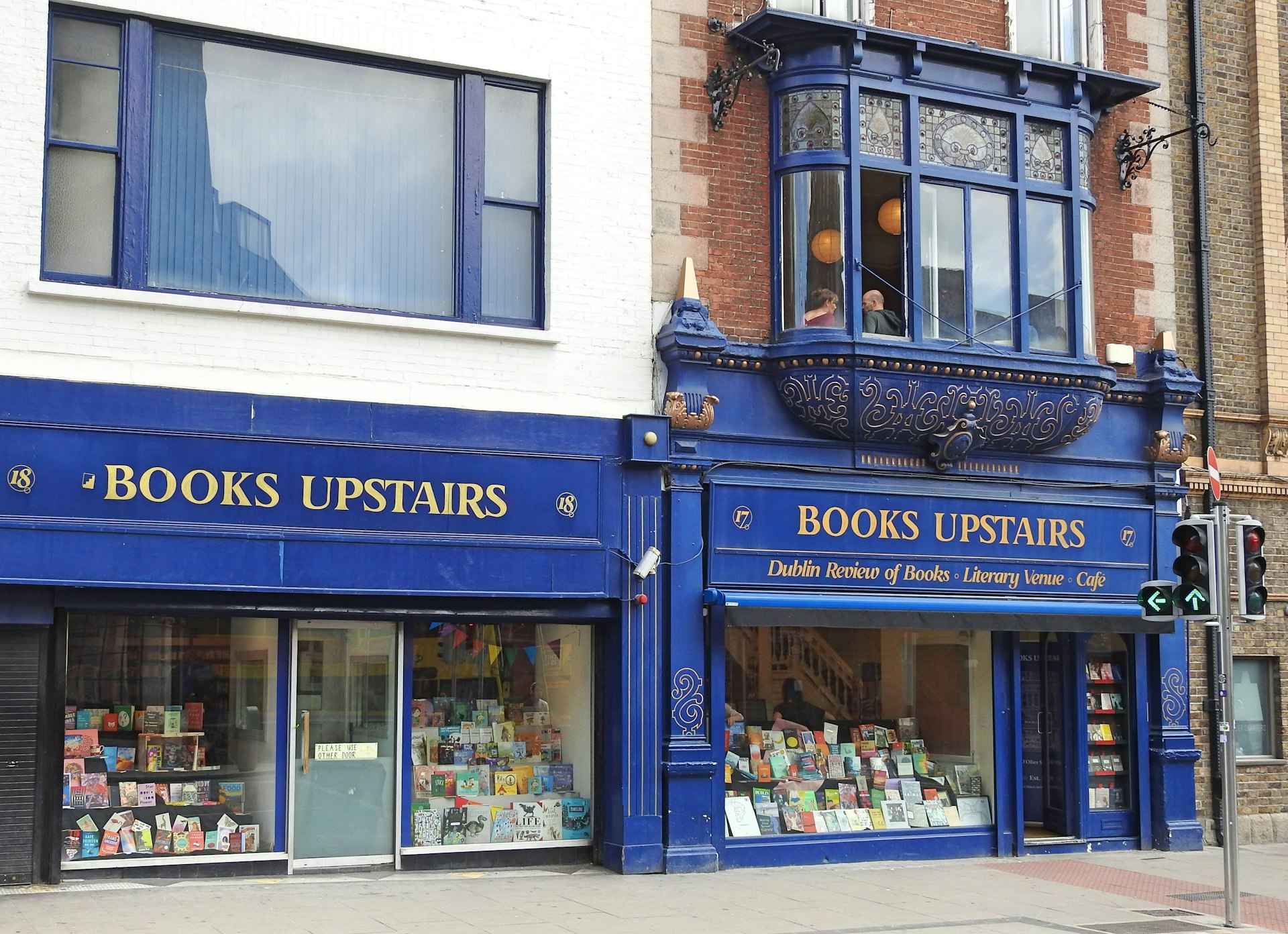 The blue fascade of a bookstore titled "Books Upstairs"