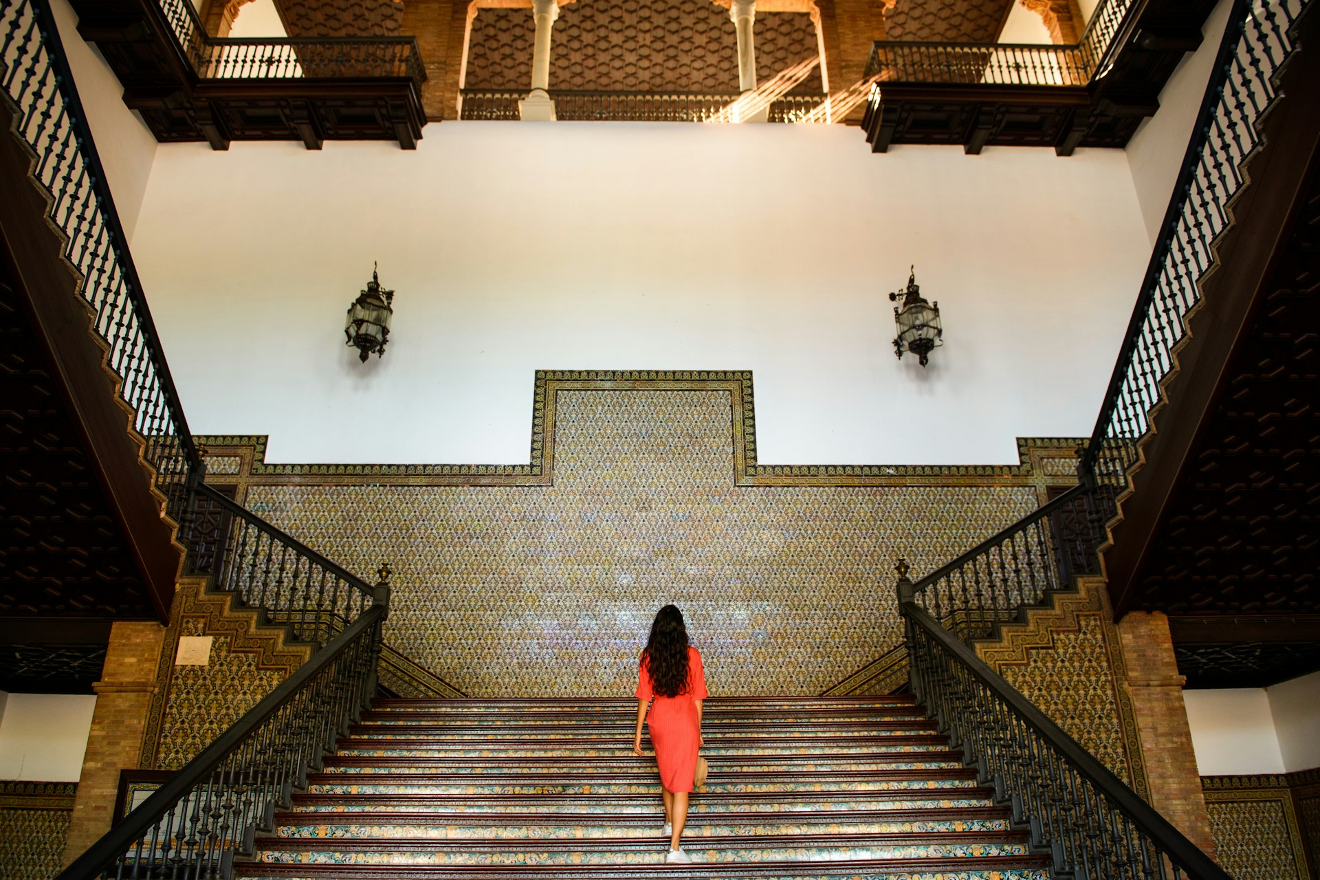 A woman walks up some steps in a building with walls covered in many tiles