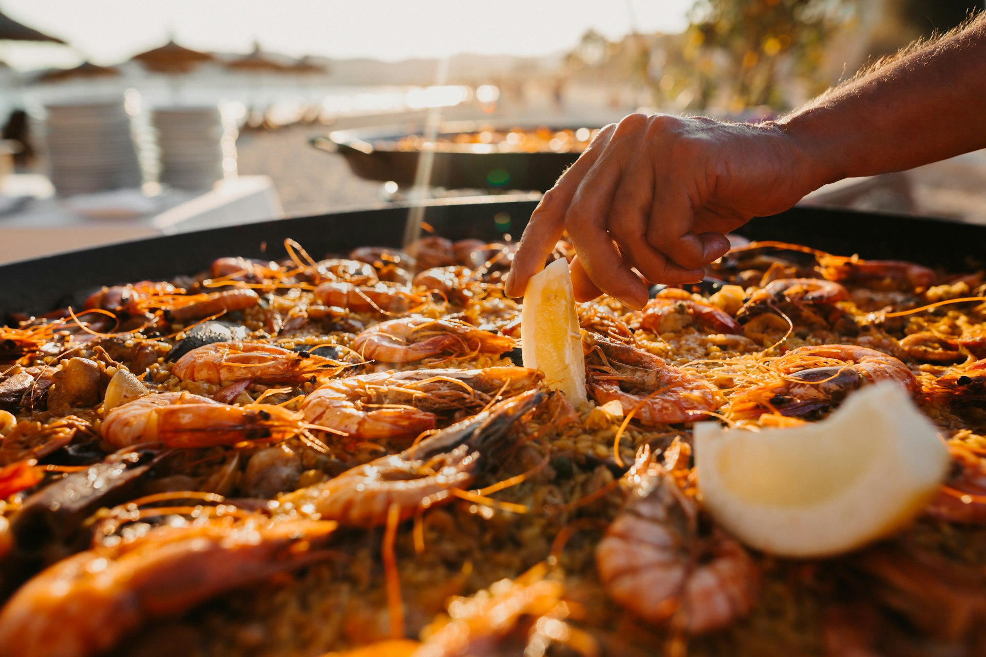 A hand reaches into a large flat pan full of rice and mussels as a paella dish is prepared