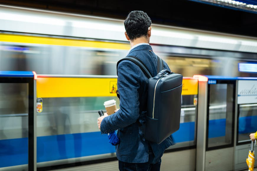 Rear view of handsome man waiting fr train at subway, holding bag on his back and cup of coffee Taipei