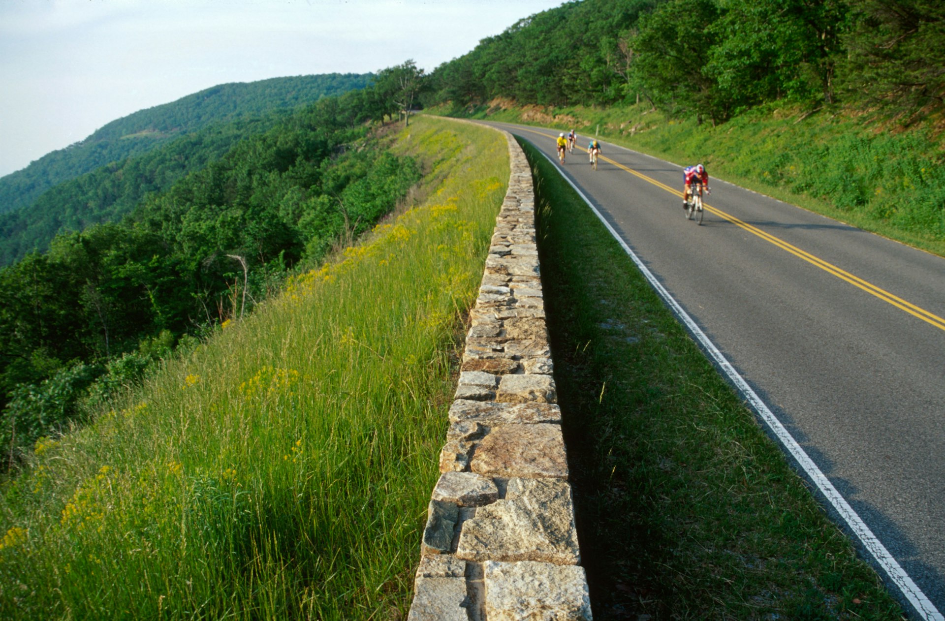 Cyclists power up a hill with hilly scenery stretching out behind them in Shenandoah National park