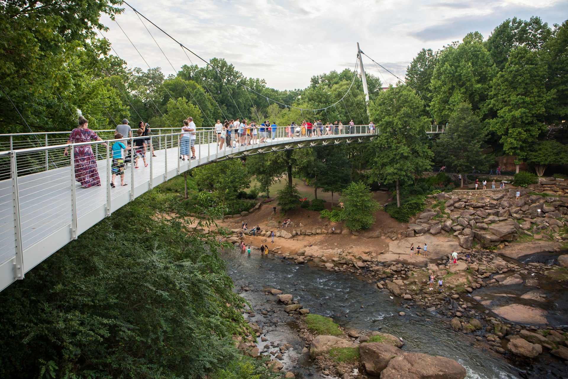 Посетители Falls Park задерживаются на мосту Свободы с видом на водопады реки Риди.