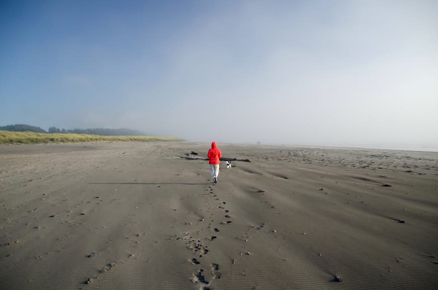A white-coated beachgoer walks along at brown sands of Seaview, on Long Beach peninsula, Washington