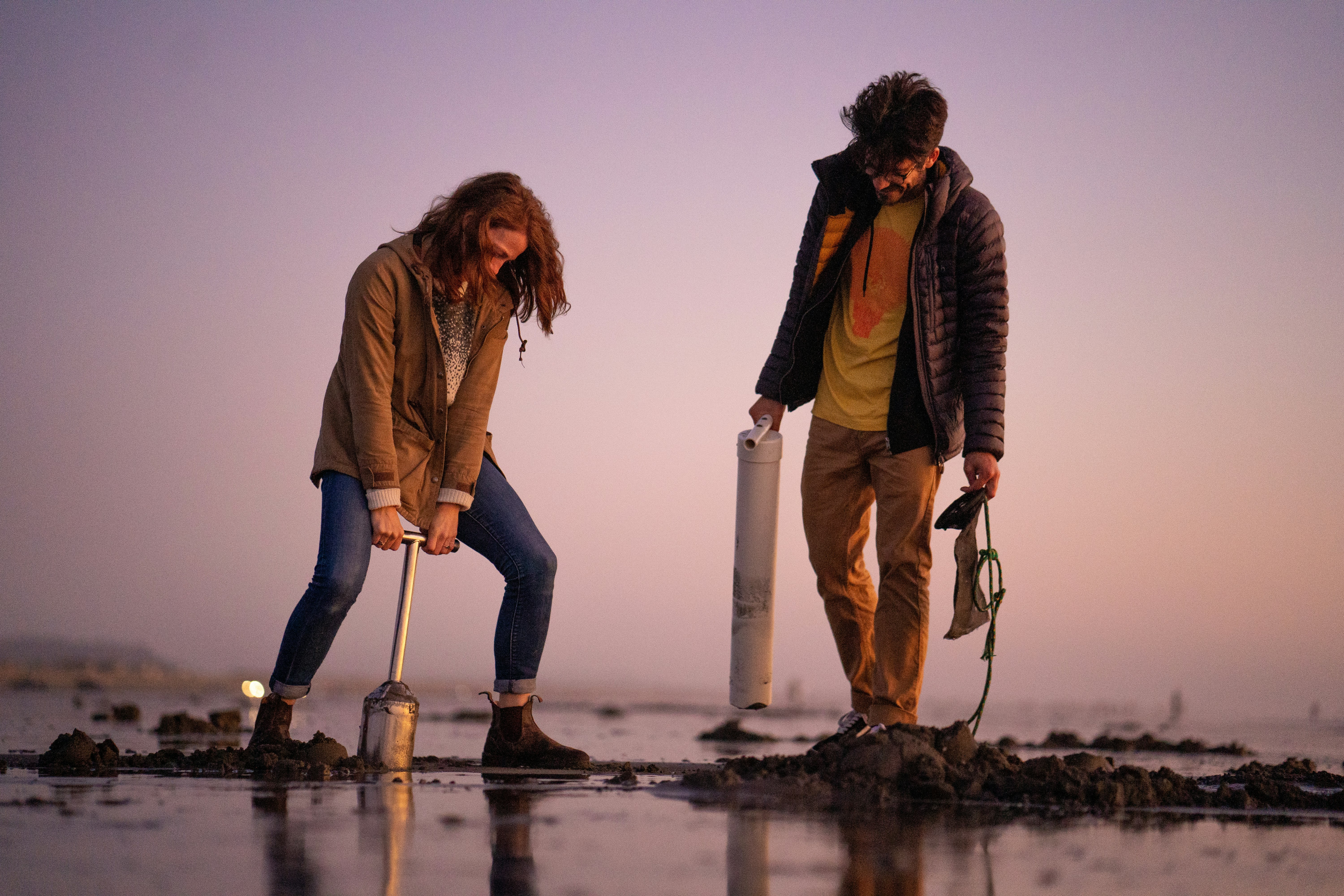 Silhouettes on the tidal flat as a white couple - a man and a woman - dig for clams on the beach at sunrise