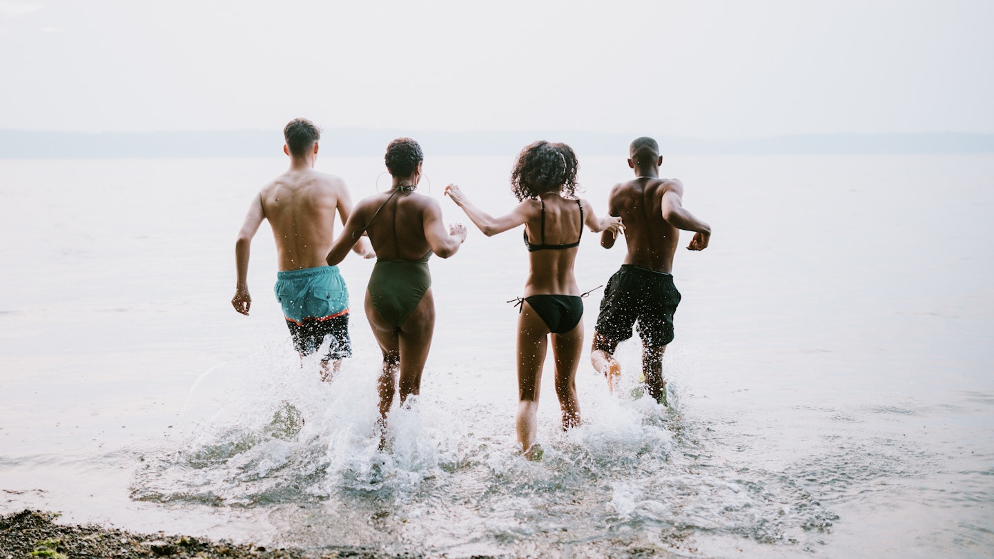 A group of teenagers play in and around the salt water of the Puget Sound, an inlet of the Pacific Ocean in Washington state, in the United States.  They splash into the cool water.