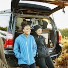 Smiling sisters hanging out at back of car after finishing backpacking trip