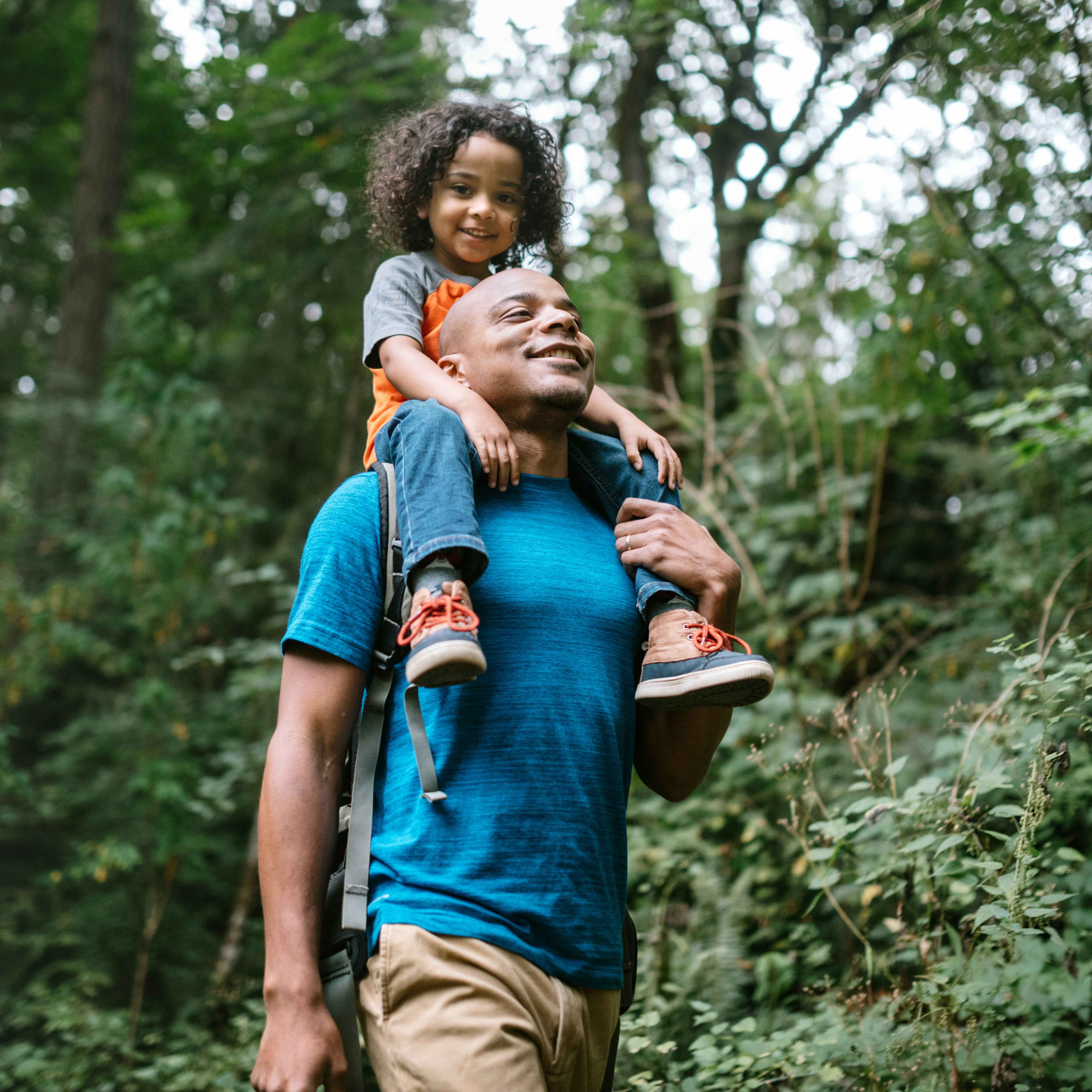 A young mixed race family spends time together outside in Washington state, enjoying the beauty of the woods in the PNW.  The dad holds his boy on his shoulders.