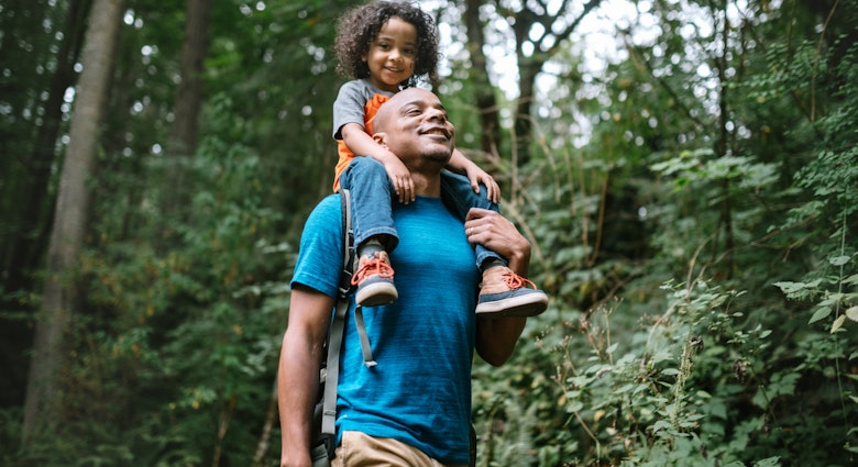 A young mixed race family spends time together outside in Washington state, enjoying the beauty of the woods in the PNW.  The dad holds his boy on his shoulders.