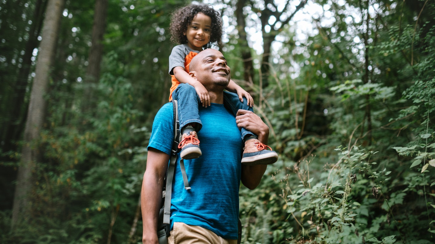 A young mixed race family spends time together outside in Washington state, enjoying the beauty of the woods in the PNW. The dad holds his boy on his shoulders.