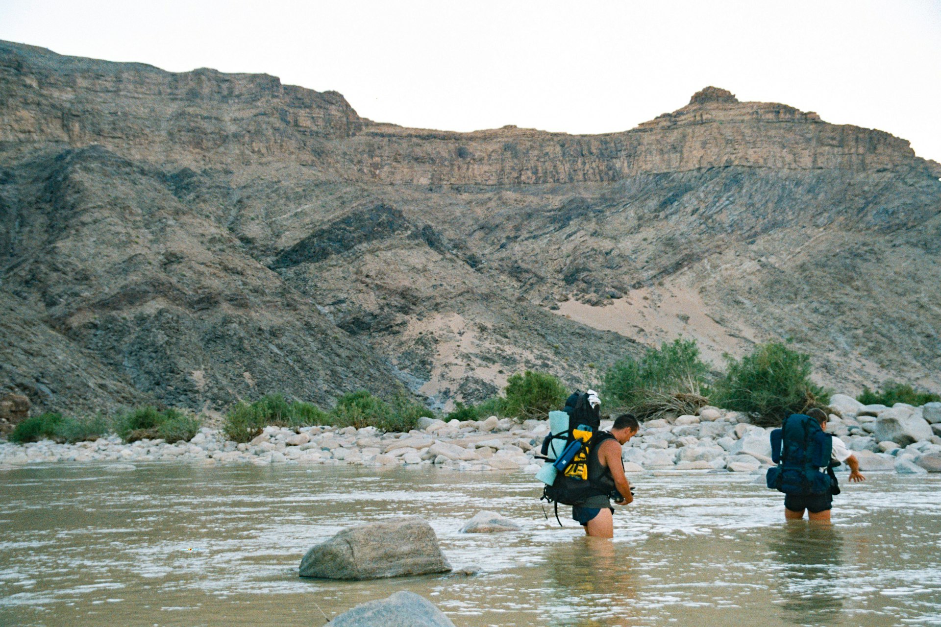 Two hikers doing a river crossing in a Canyon