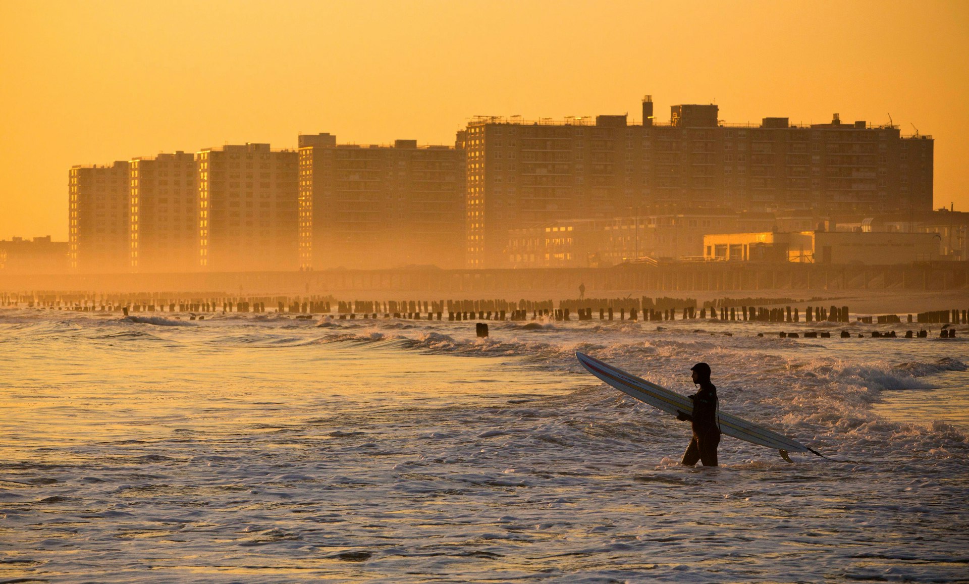 A surfer walks out into the ocean at Rockaway Beach