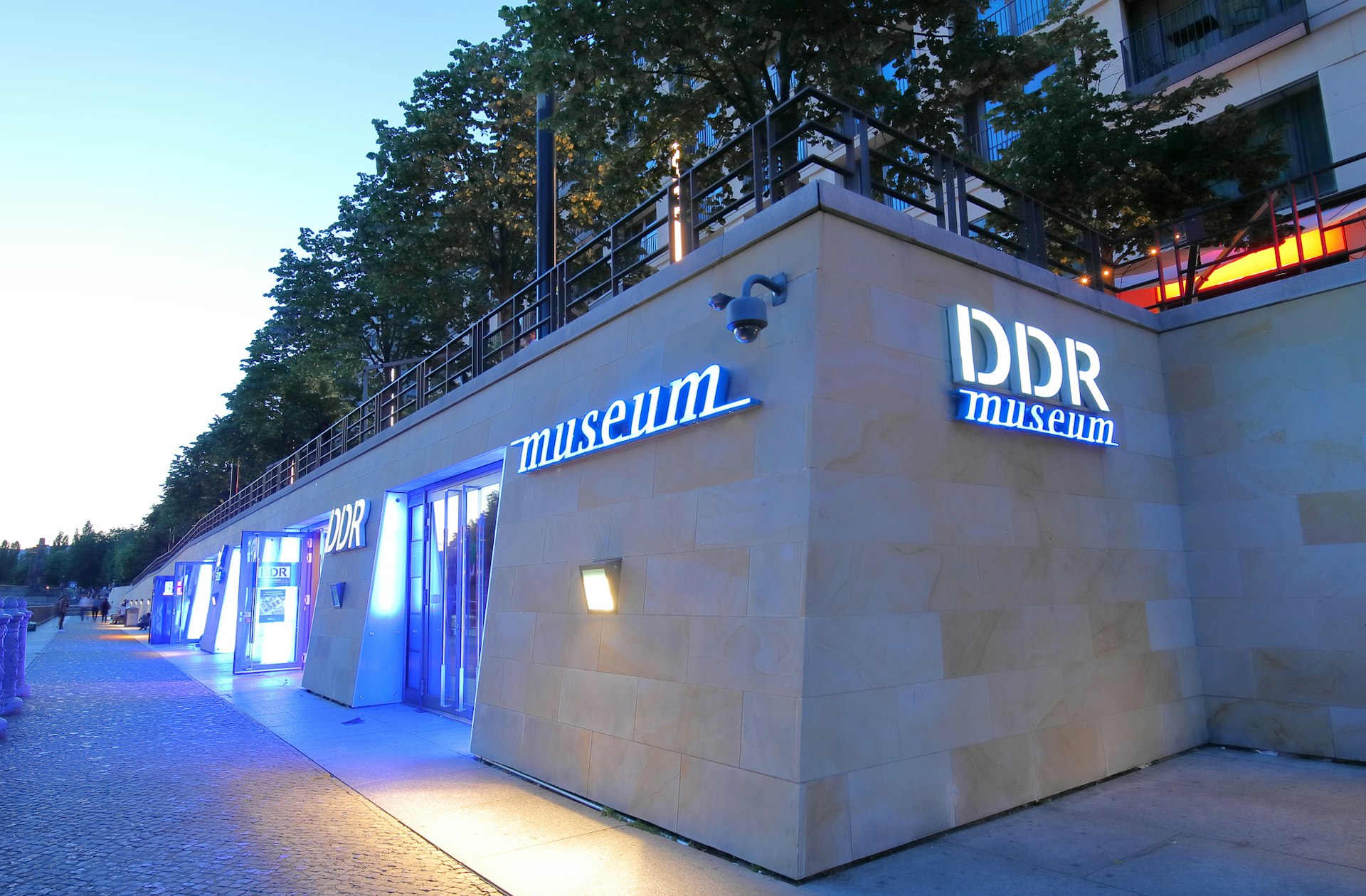 The exterior of the DDR Museum in Berlin, lit up with blue lights at night 