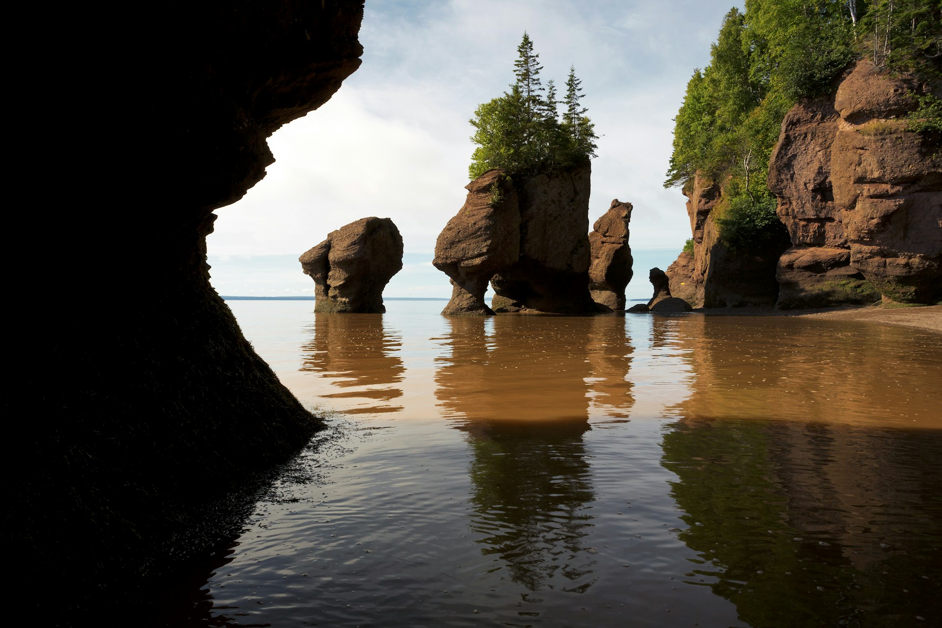 Water laps against some coastal rock stack formations in a quiet cliff-lined bay