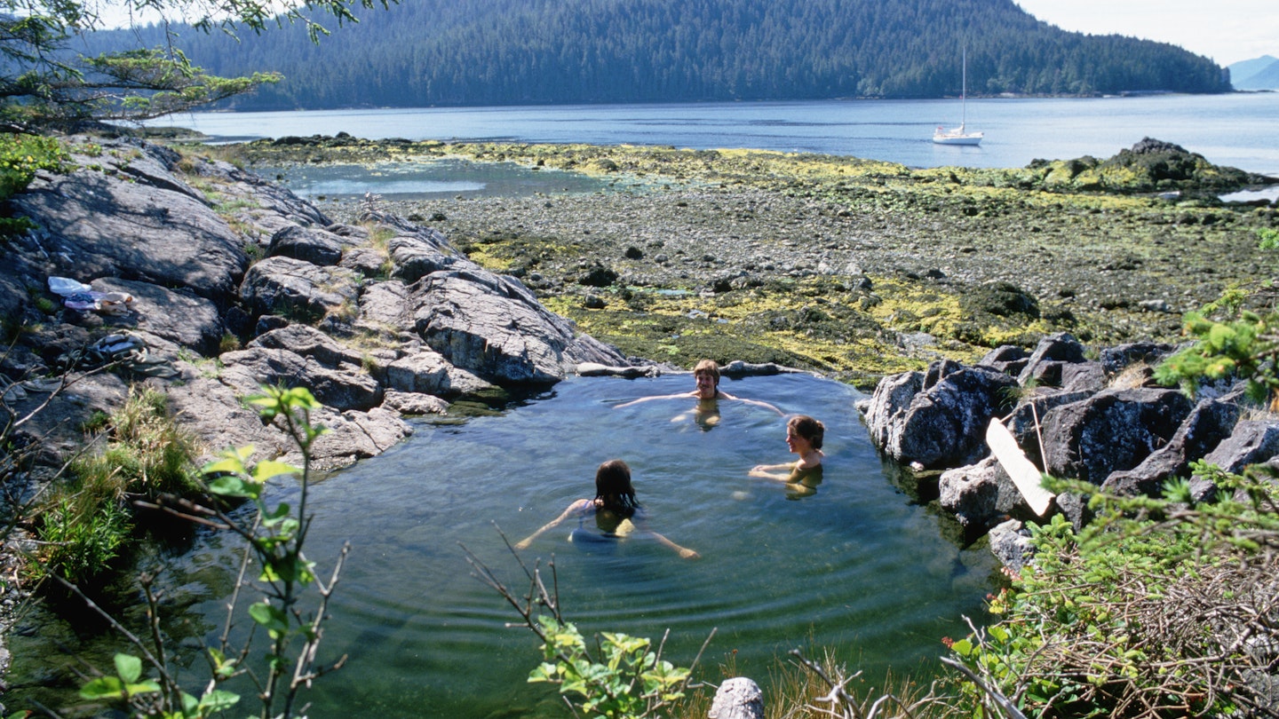 Three women enjoy a soak in a hot spring overlooking Hotsprings Cove on one of the Queen Charlotte Islands.
