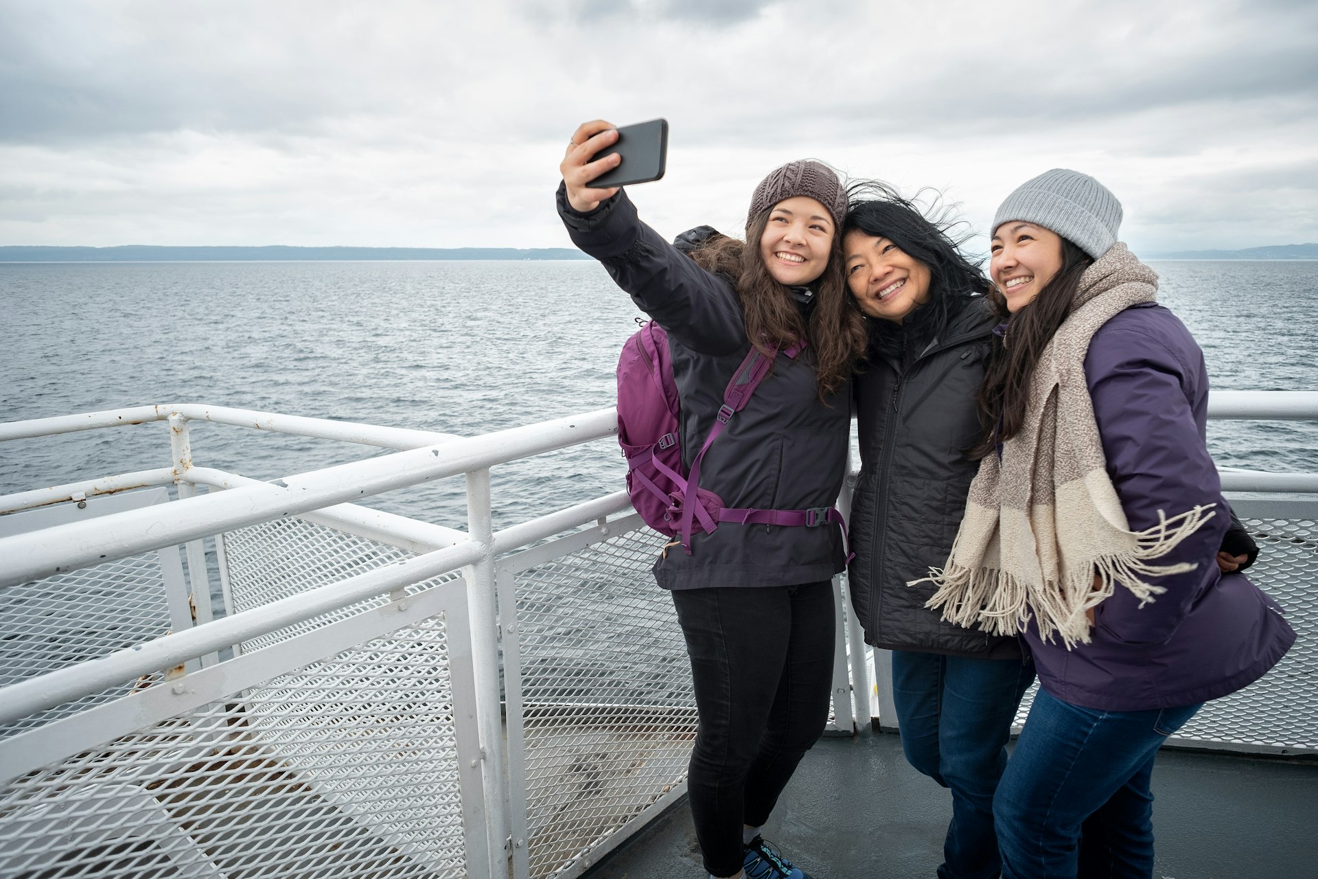 A family of a mother and two teen daughters take a selfie on a ferry