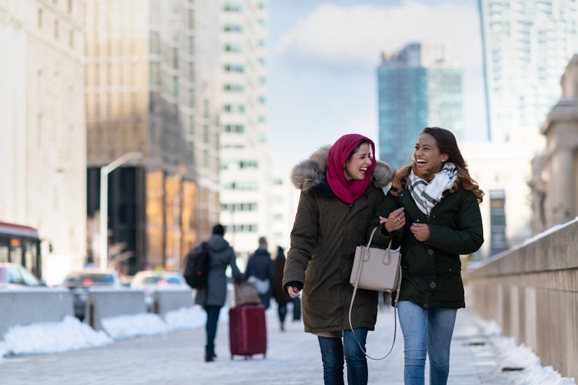 Two (2) attractive muslim adult female friends smile as they walk through the city. They are stylish and enjoying a cold winter stroll together.