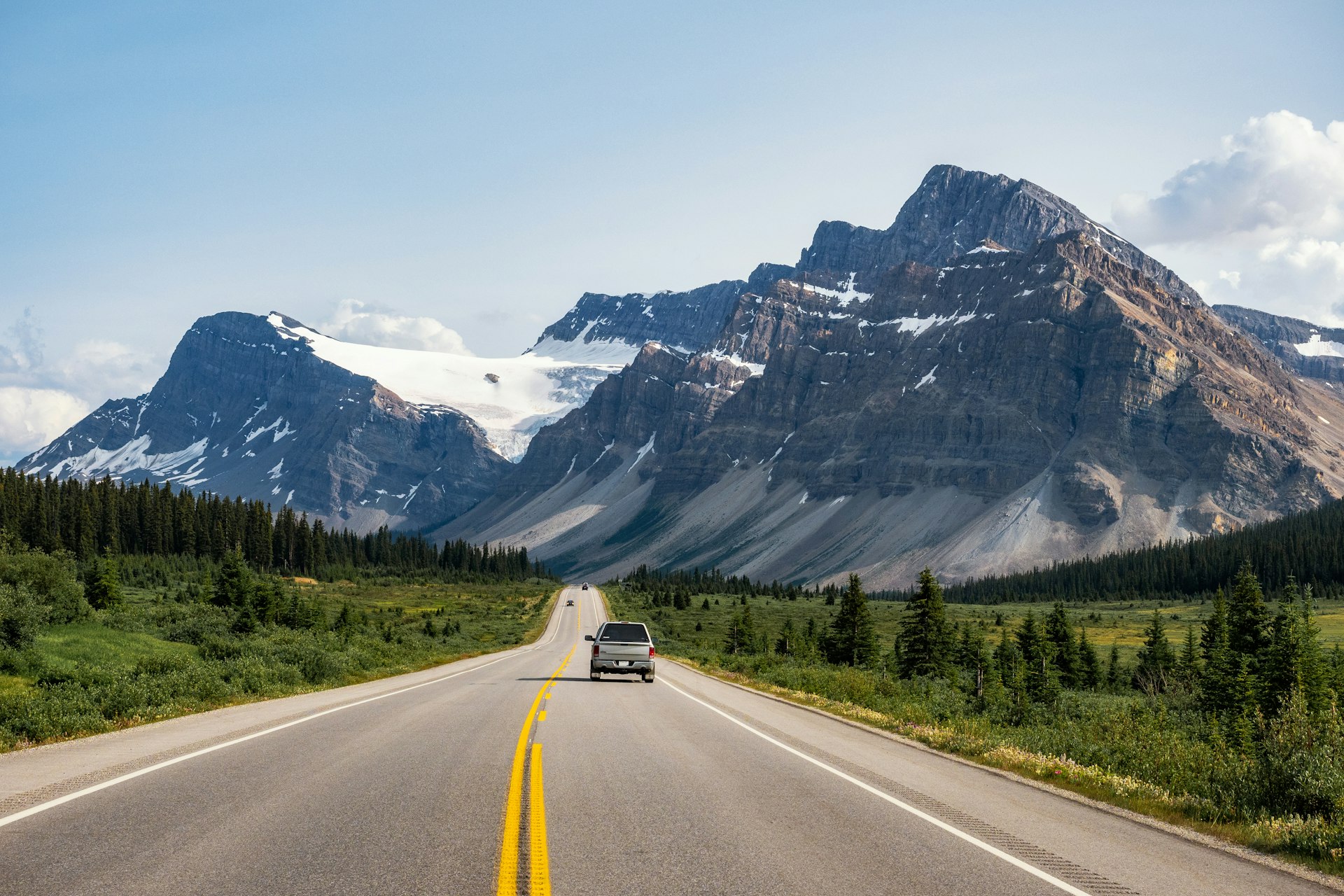 A car travels along a highway towards huge mountain peaks in Canada