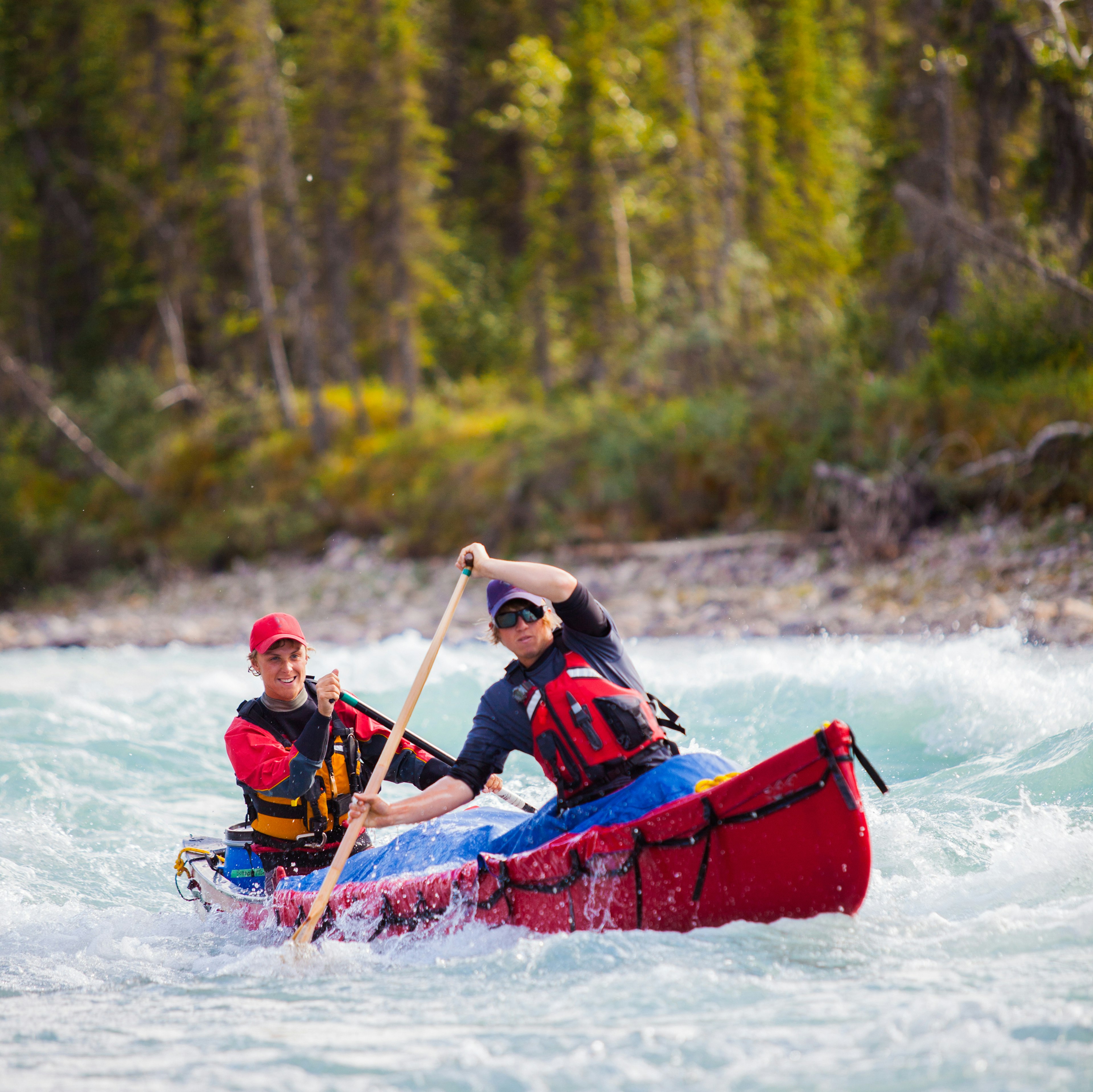 Two people paddle a canoe in a river in Northern Canada