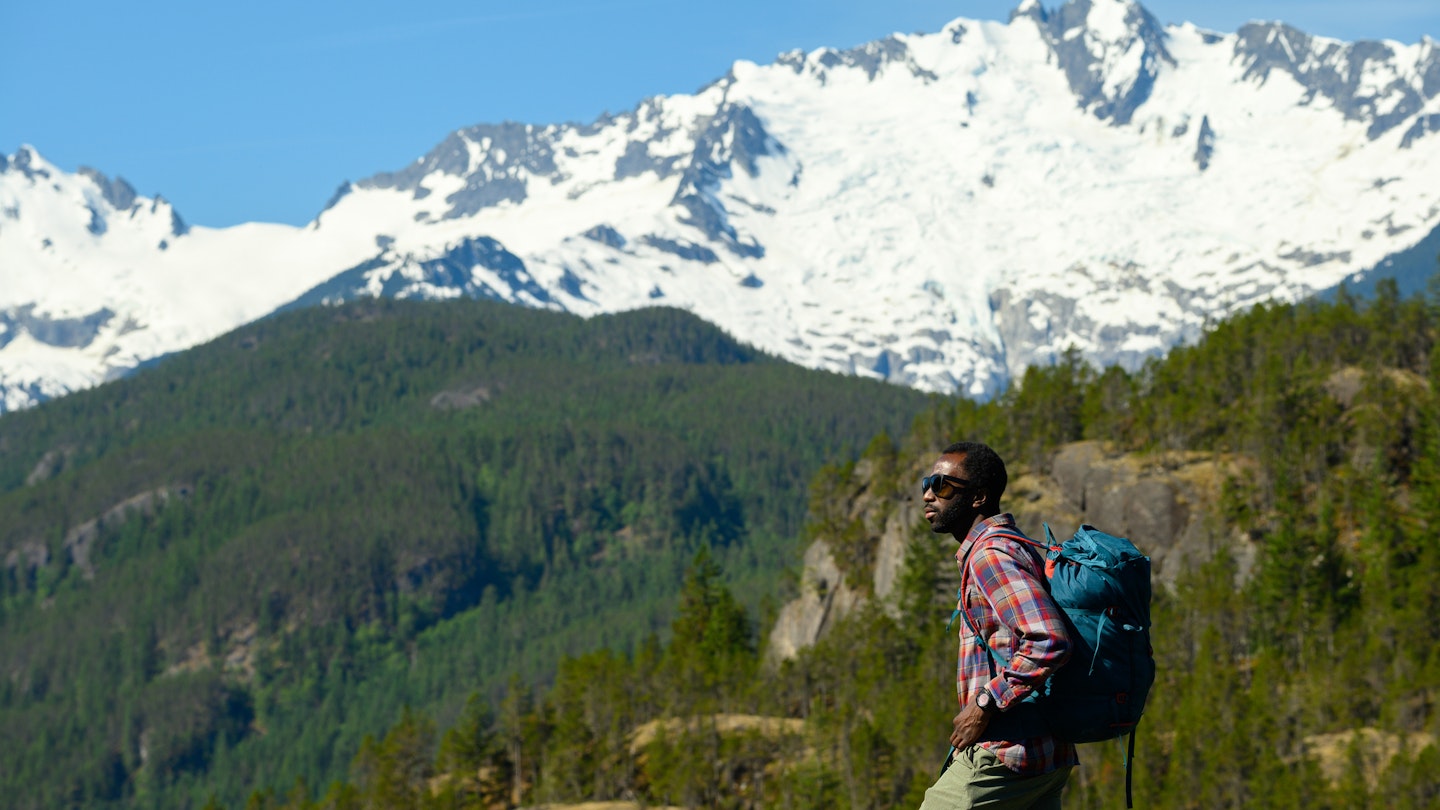 Male hiker looking away while standing against mountains. Mid adult man is spending vacation in forest. He is wearing sunglasses and casuals.