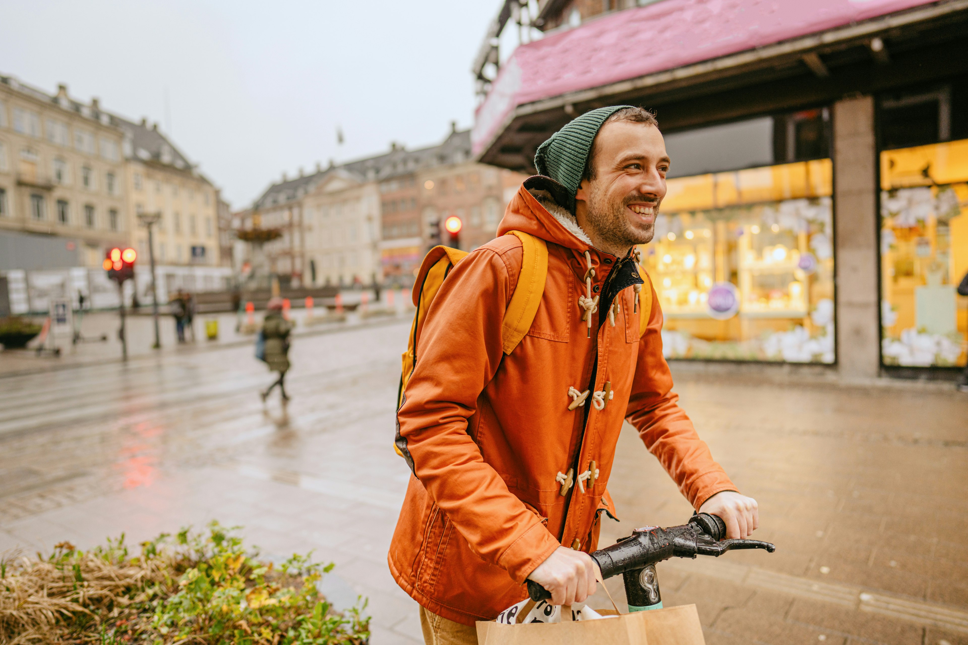 A smiling man rides an electric scooter through a city square