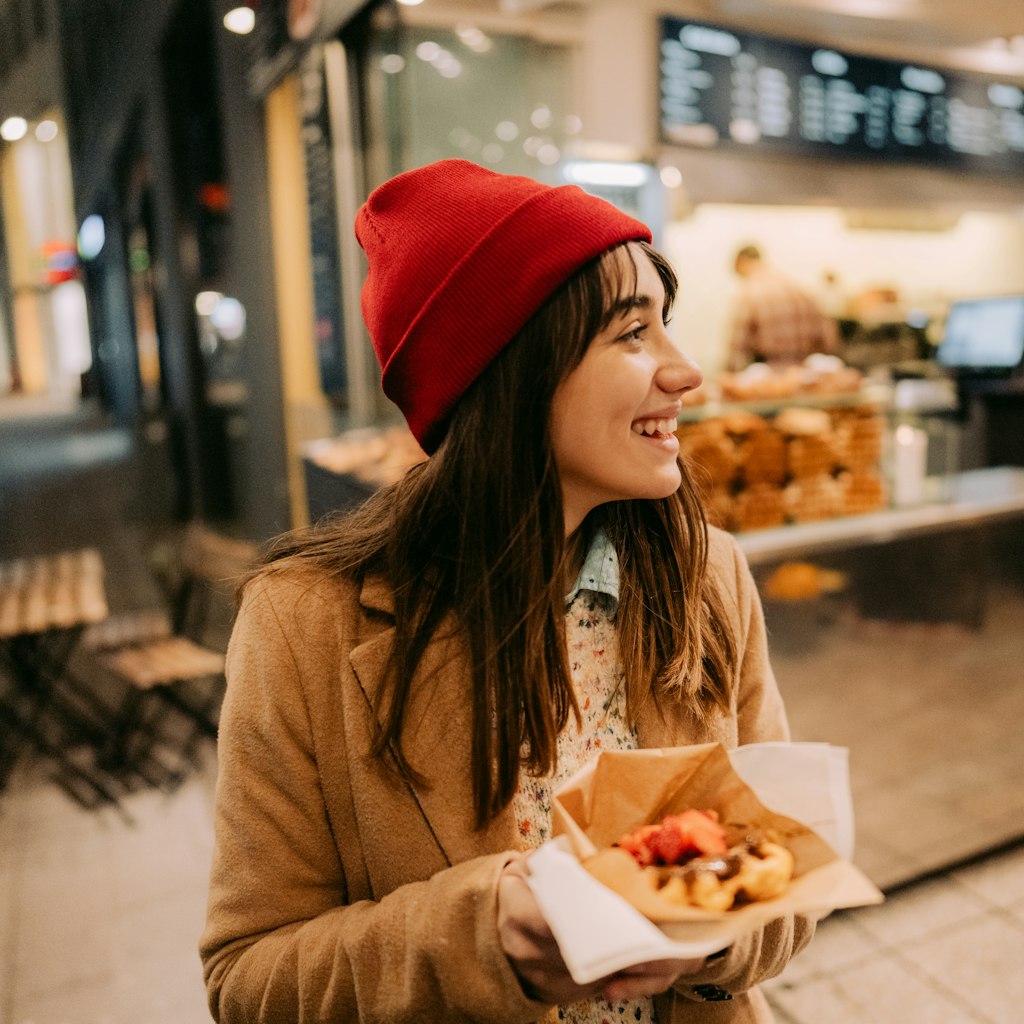 Photo of a young woman trying out different kinds of street food, and having a meal on the go.