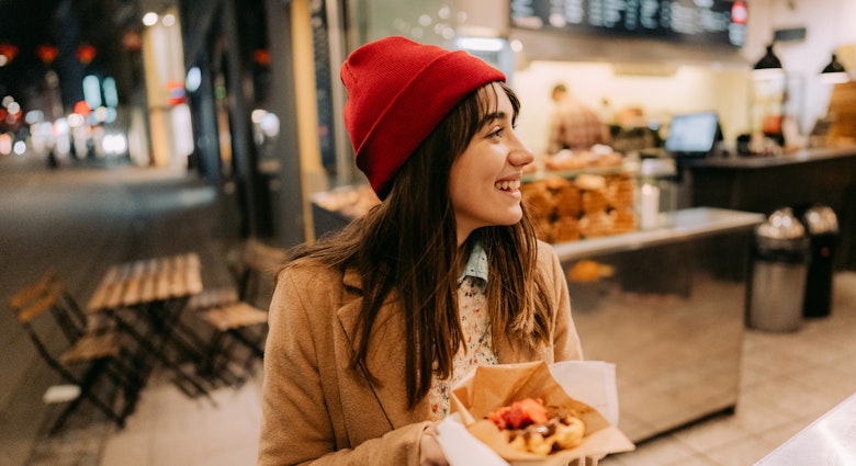 Photo of a young woman trying out different kinds of street food, and having a meal on the go.