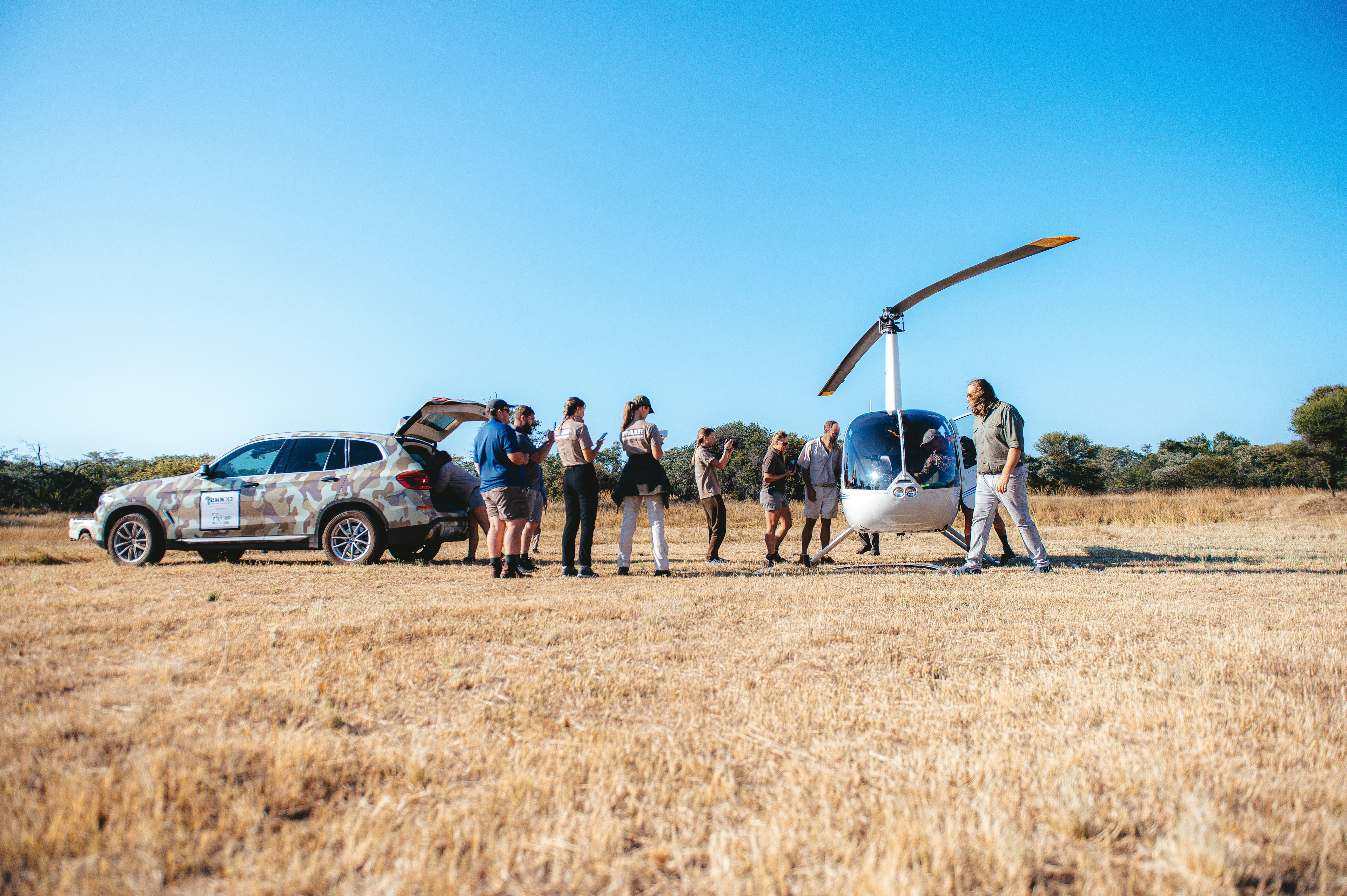 A group of park rangers and researchers stand next to a helicopter parked in a savannah in South Africa.