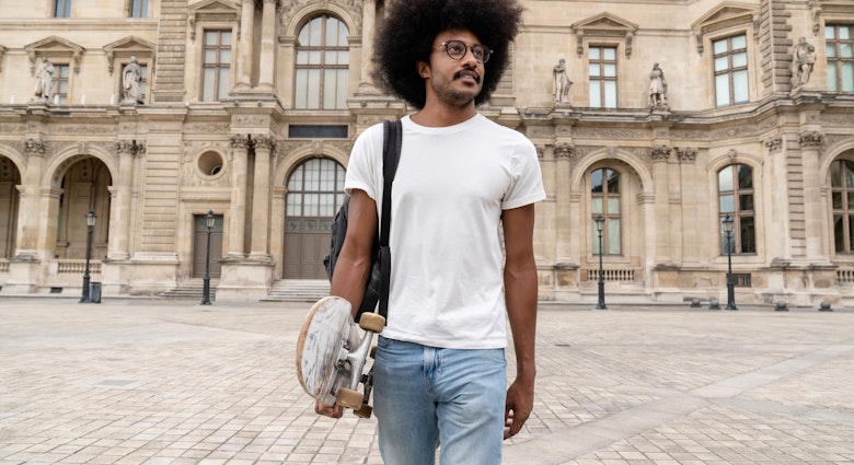 Hipster man with afro hair walking on the street of Paris. He is carrying skateboard.

