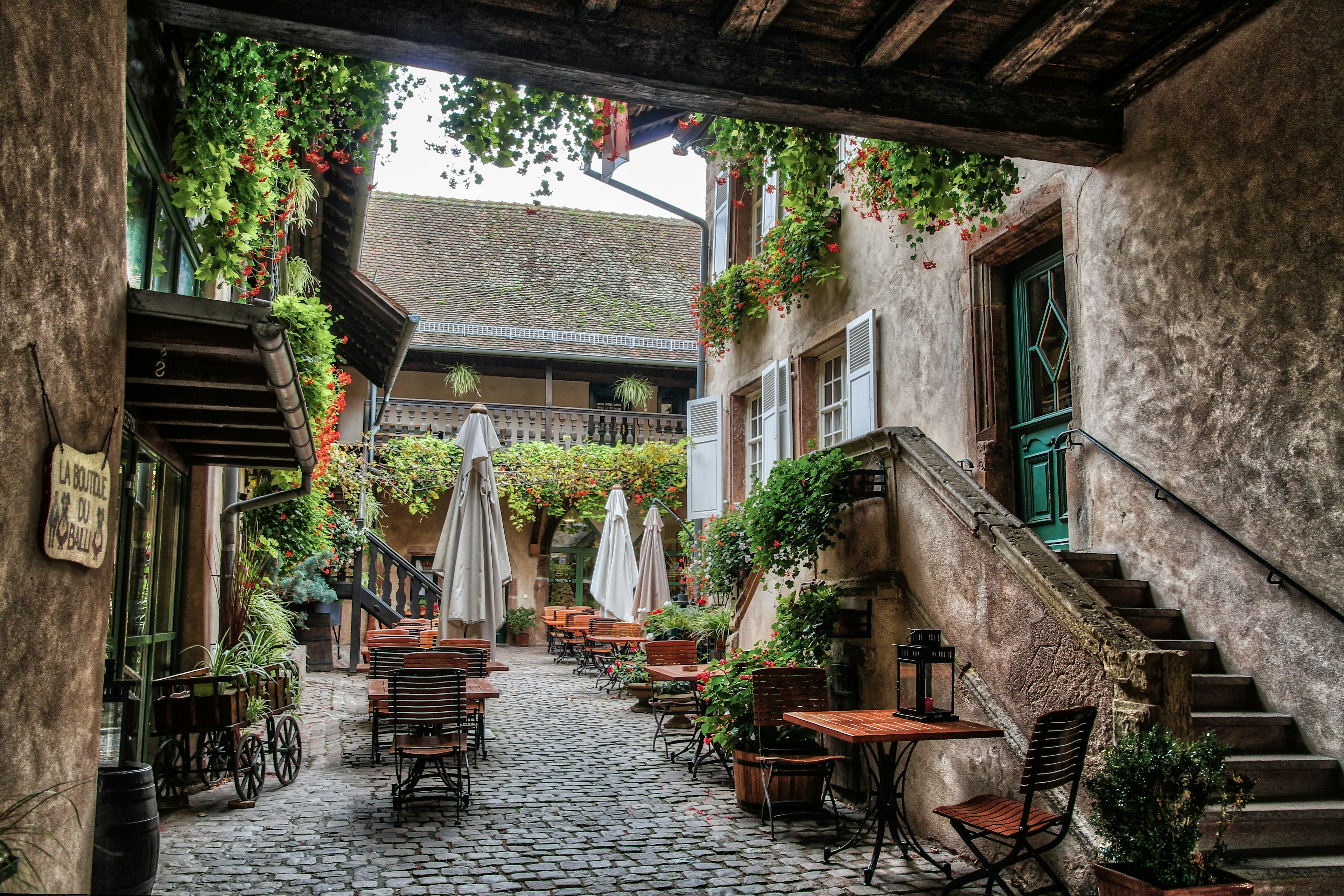 A courtyard of a large stone building covered in greenery with chairs and tables