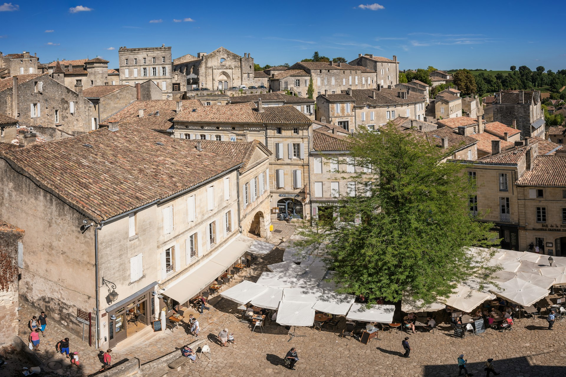 Top view of St Emilion square, a very touristic village in the vineyards of the Bordelais. People are enjoying a meal under umbrellas in the square.