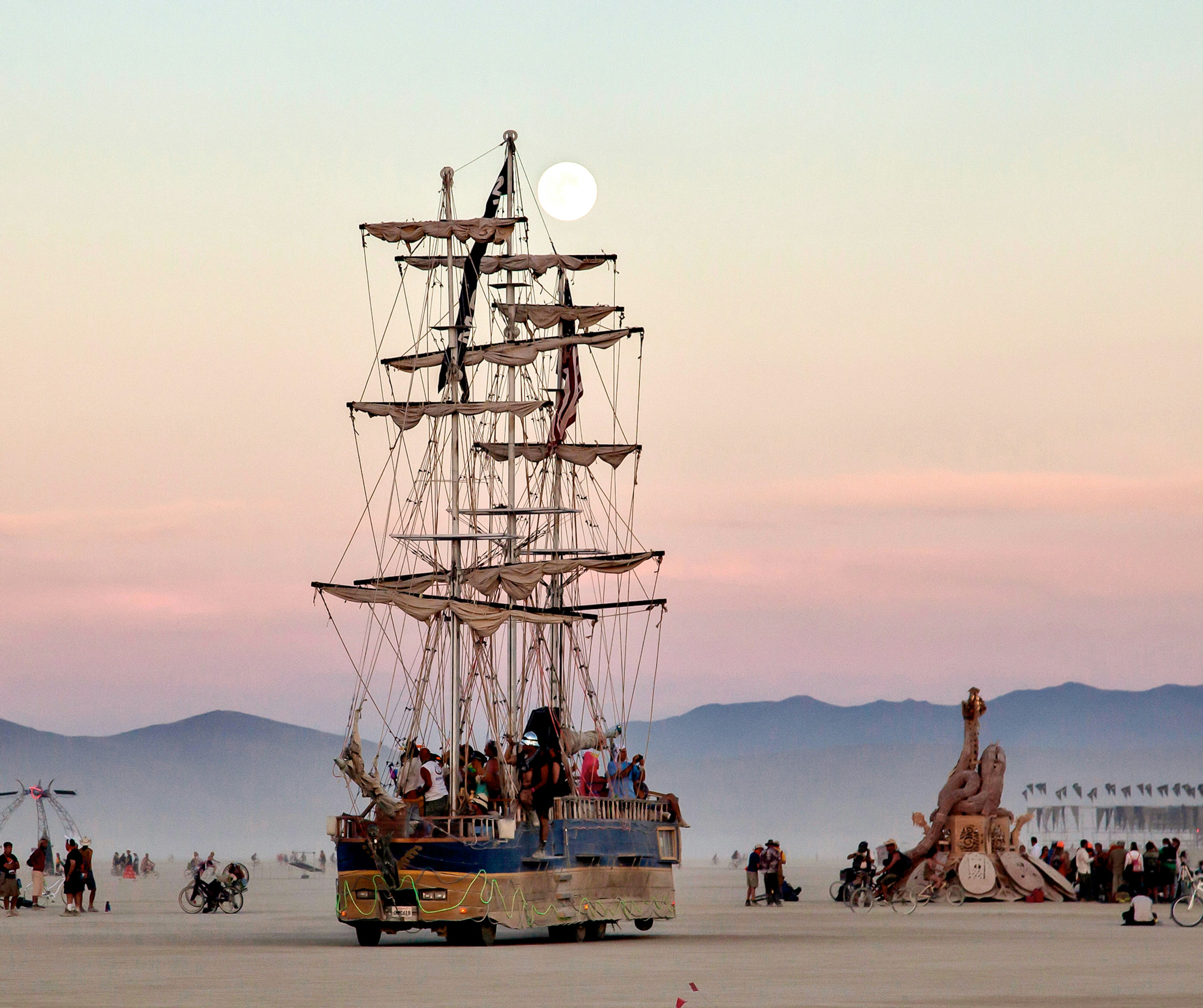 A tall sailing ship coasts the playa at sunset