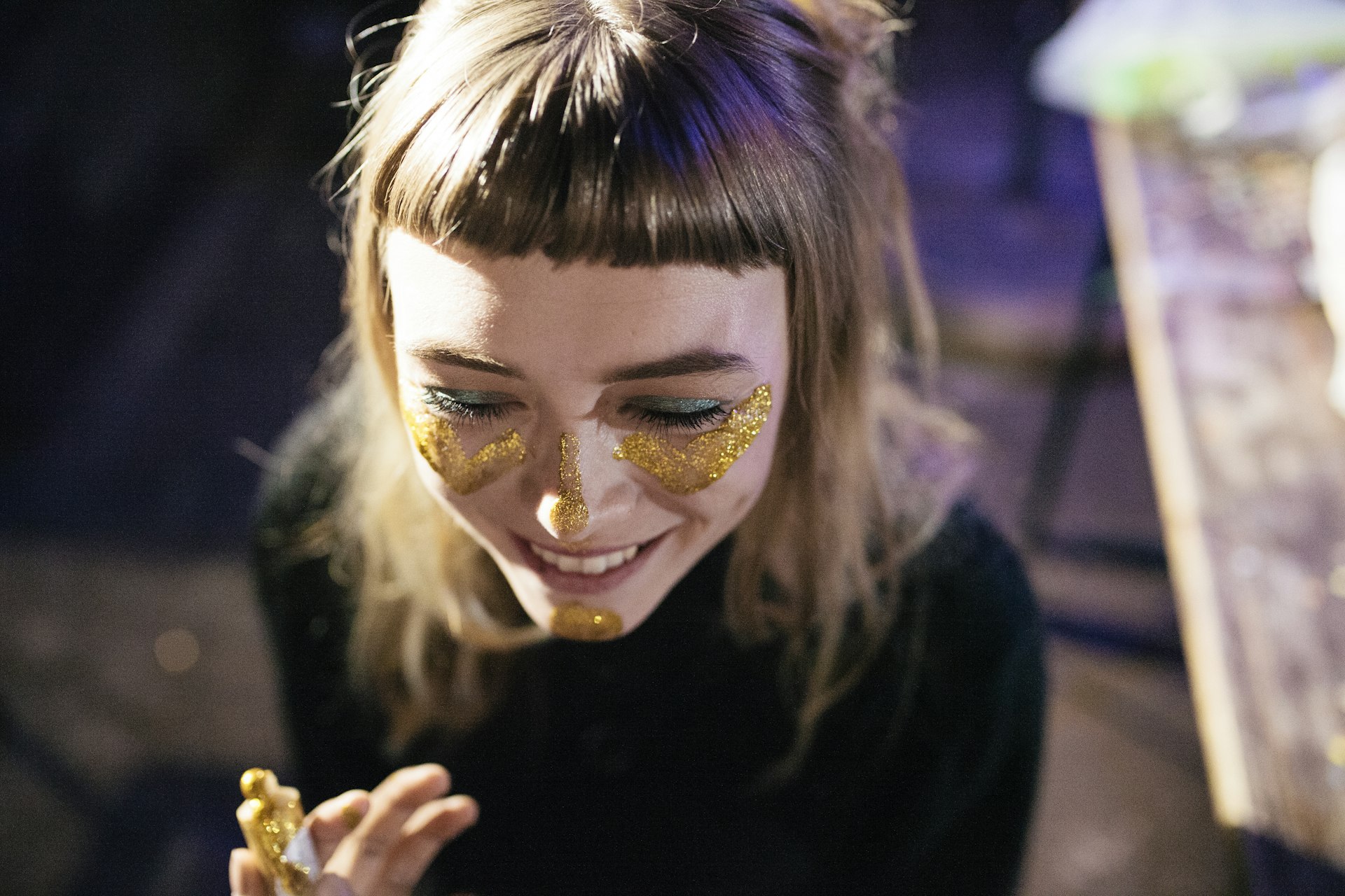 A woman smiles as she paints her face with gold glitter while out clubbing