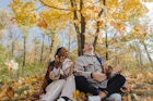 A couple sitting on blanket in park in autumn and throwing leaves up in the air