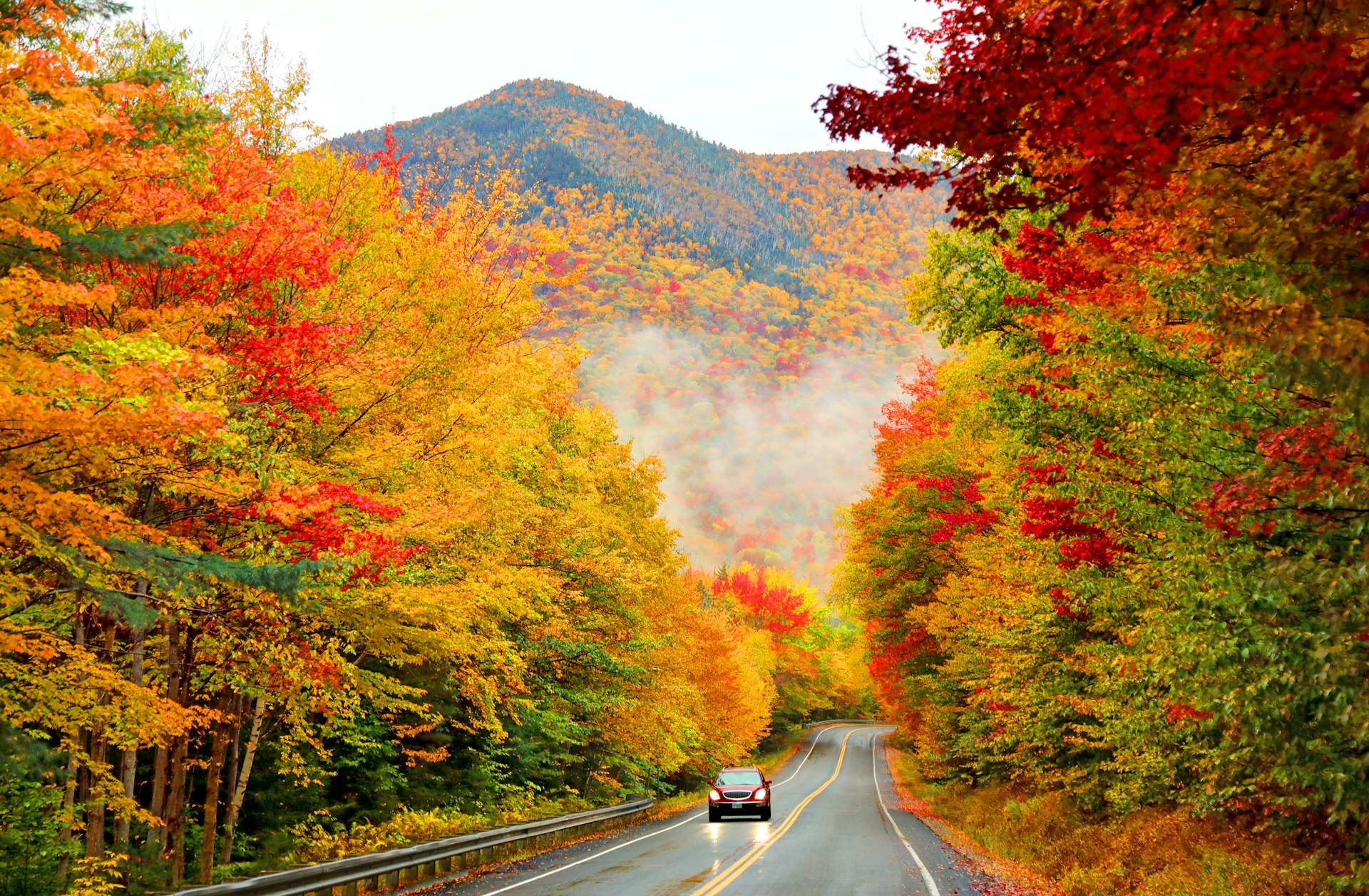A car drives through fall foliage along the Kancamagus Highway, New Hampshire, New England, USA
