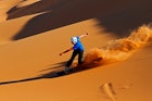 A trail of sand is visible in the late afternoon sun when this sandboarder speeds down the dunes of Swakopmund, Namibia.