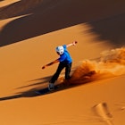 A trail of sand is visible in the late afternoon sun when this sandboarder speeds down the dunes of Swakopmund, Namibia.