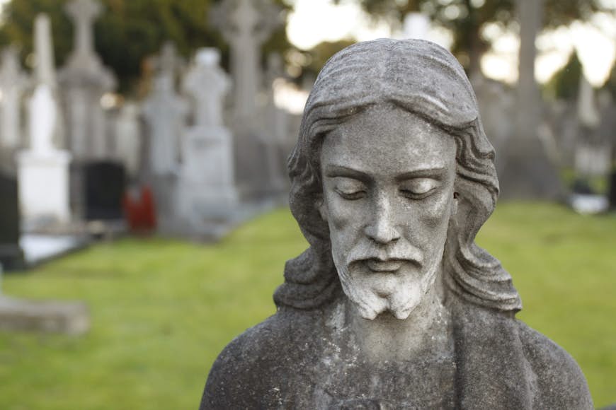 A stone statue of a man marks a grave site in a cemetery